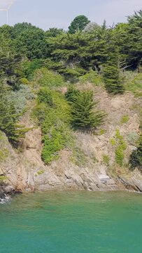 Aerial view of rugged coastal cliffs covered with dense green vegetation rising above clear turquoise waters in Brittany, France.