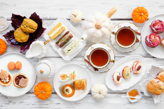 Autumn theme afternoon tea table scene over a white wood background. Pumpkin and apple theme savory finger foods, sandwiches, scones, and desserts. Overhead view.