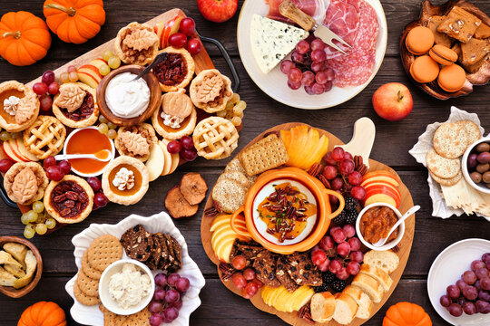 Autumn or Thanksgiving appetizers, sweets and grazing boards. Top view table scene on a dark wood background. Pumpkin and apple snacks, charcuterie, pies, desserts.