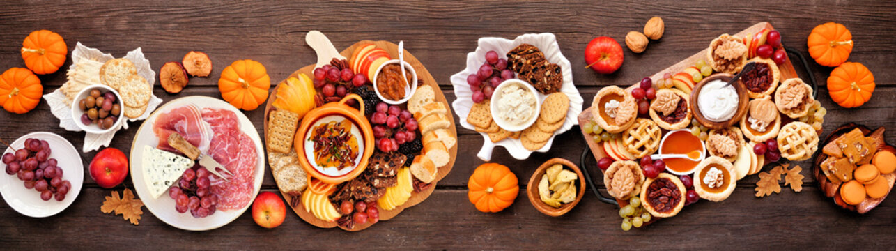 Autumn or Thanksgiving appetizers, sweets and grazing boards. Above view table scene on a dark wood banner background. Pumpkin and apple snacks, charcuterie, pies, desserts.