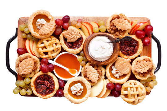 Autumn pie theme dessert board. Top down view isolated on a white background. Pumpkin, apple and pecan mini pies, with whipped cream, caramel and fruit.
