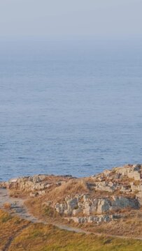 Wide shot of the rugged rocky coastline and dry grass on Ilot Saint Michel, with the calm blue sea stretching into the distance in Brittany, France.
