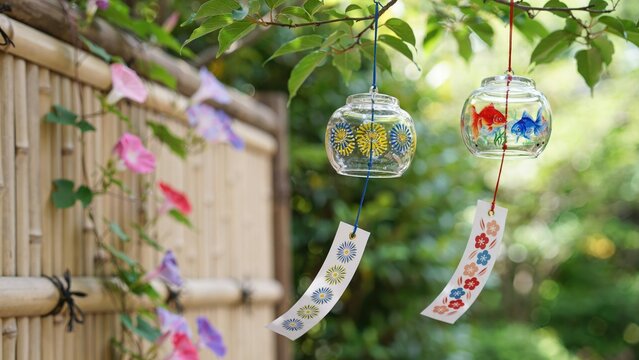 Two japanese glass wind chimes with painted fish and flowers hanging in a garden
