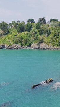 A scenic coastal view of the cliffs in Binic, Brittany, France, showing lush green vegetation atop rocky cliffs and turquoise sea water below.