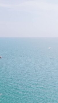 A wide view of a sailboat gliding across calm blue waters near the rocky cliffs of Binic, Brittany, France.