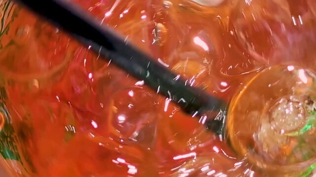 Close-up of orange drink swirling in a glass with black straw, showing liquid movement, reflections, bubbles, and fresh texture. Slow motion footage for beverage and summer concepts.