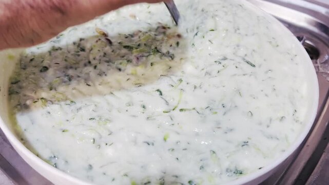 Stirring Persian yogurt cucumber dip with spoon close up 16:9, homemade appetizer food concept