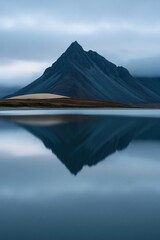 Fototapeta premium Sharp triangular mountain mirrored in glassy water for calming lake wallpaper and vertical nature background design