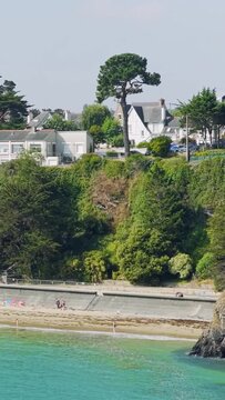 A scenic coastal view in Binic, Brittany, France, featuring lush green cliffs, beachfront houses, and a sandy beach with turquoise water.