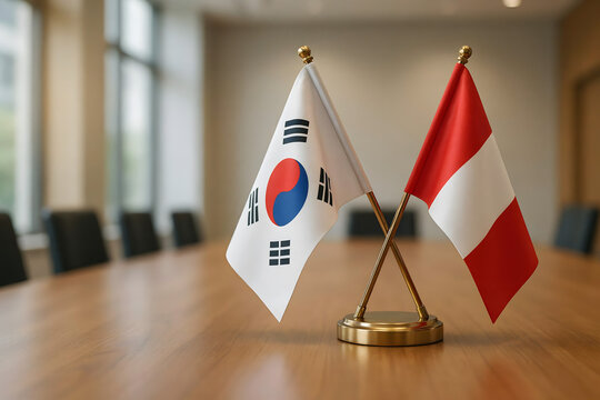 Miniature flags of south korea and peru crossed on a golden stand on a wooden office desk with a blurred meeting room in the background