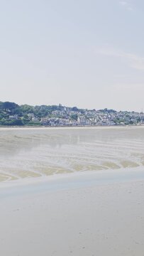 Wide shot of a sandy beach at low tide with tidal patterns in the sand, facing the coastal town of Binic in Brittany, France.