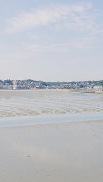 A wide, tranquil view of Binic beach and town in Brittany, France, captured during low tide on a bright summer day.