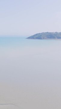 A serene wide shot of Binic beach in Brittany, France, showing calm shallow water and a distant green headland under a clear summer sky.