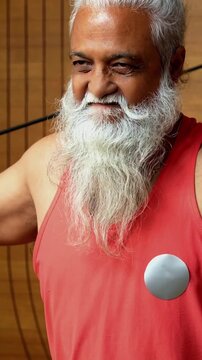 Indian mid age stylish bearded man doing exercise using resistance band at home, fitness conscious mature male showing strength, agility and determination during workout in modern interior