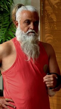 Indian mid age stylish bearded man doing exercise using resistance band at home, fitness conscious mature male showing strength, agility and determination during workout in modern interior