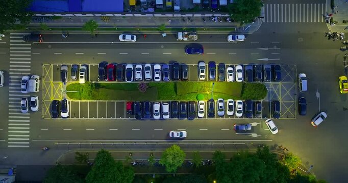 Nighttime aerial view of a busy parking area and multilane street in Nanjing, China, with parked cars, traffic, crosswalk, trees, and urban lighting.