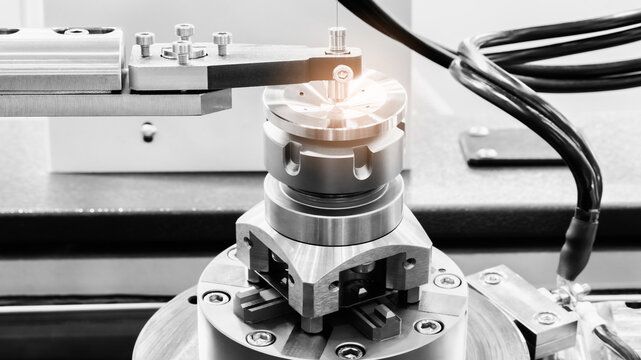 Close-up of metallic mechanical assembly. Cylindrical component secured by screws and bolts. Electrical wires connected to device. Industrial precision machine part visible