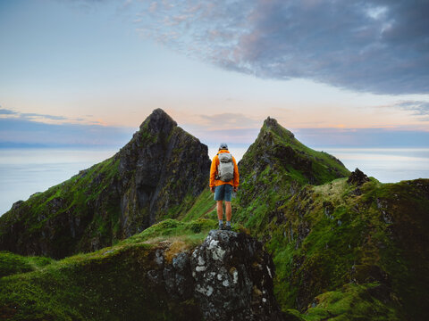 Traveler man explore Norway hiking mountains travel solo in Lofoten islands, healthy lifestyle active adventure summer vacations trip outdoor hiker tourist standing on cliff with backpack freedom