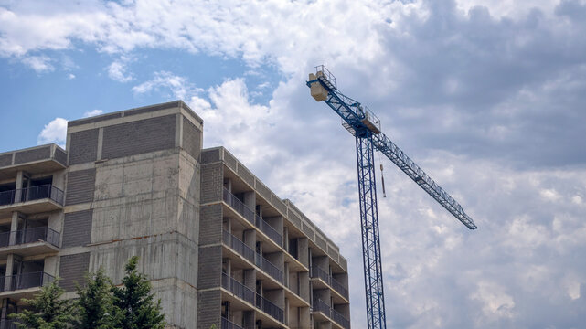 Concrete building under construction with a blue tower crane against a cloudy sky, symbolizing urban development, progress, and the ongoing growth of a modern cityscape