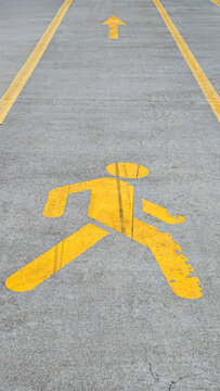 Yellow pedestrian symbol on concrete path with forward arrow and guidance lines, representing progress, movement, direction, and safety for walking
