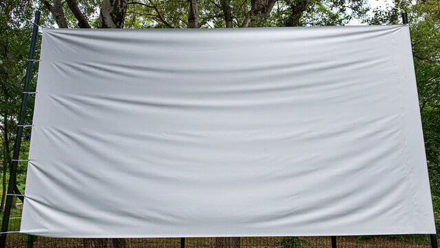 Blank outdoor projection screen hanging in a park, ready for content, showing copy space, concept of open air cinema, advertising, or presenting ideas in nature