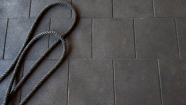 Battle rope resting on black rubber gym flooring, representing power, endurance, and physical challenge in a dedicated training environment