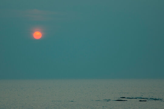 Minimalist moody sunset over calm sea with red sun and teal copy space
