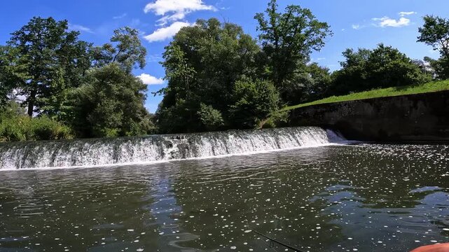 POV fisherman casting lure into river current below a small dam, active freshwater sport fishing