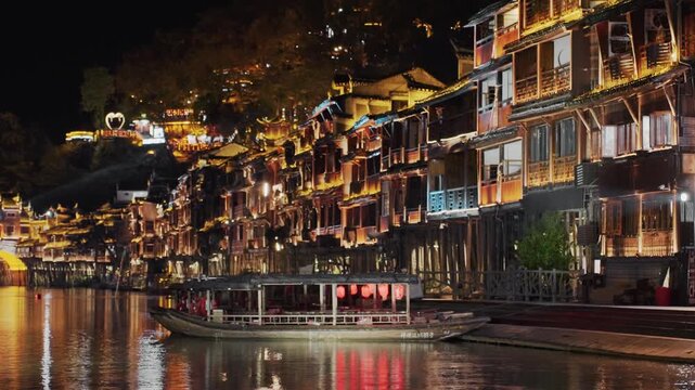 Night waterfront lined with lights, multistory riverside buildings adorned with glowing windows and balcony lanterns, docked boat casting shimmering reflections, cozy cafs and terraces, bustling