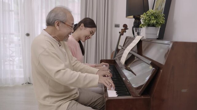 Happy Asian senior elderly father and his beautiful daughter sit playing piano and singing together having fun and enjoying in living room at home. Lifestyle and leisure after retirement with family. 