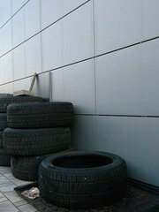 Stack of used car tires against a modern grey building wall © Svetlana