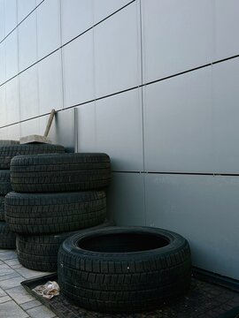 Stack of used car tires against a modern grey building wall