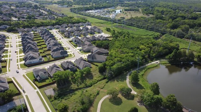 Newer master planned home developments sit adjacent to retention ponds paved walking trails in Lyons Crest Estates in Dallas Fort Worth suburbs. Power line corridors stretch past open Garland, TX