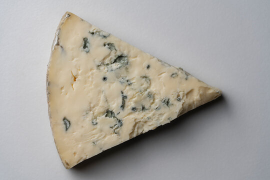 Triangular wedge of gourmet blue cheese on white background, closeup. Top view of single piece of premium blue mold cheese with visible veins on clean light surface