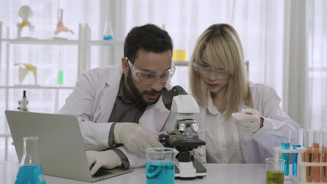 Two professional scientists and researchers are excited and happy about their success in conducting chemistry experiments on a medical vaccine, using a microscope and laptop in the science laboratory.