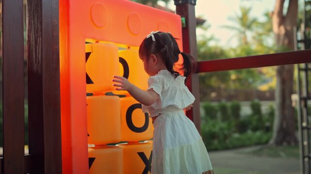 Young girl playing with giant tic tac toe game outdoors, turning blocks during playful childhood activity