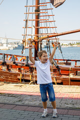 Happy little boy playing near an old wooden sailing ship at the harbor, enjoying a fun summer vacation by the sea and city waterfront © Дмитрий Швец