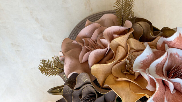 Close-up of elegant artificial floral arrangement in soft pink, beige, brown and gold tones on a light marble surface with copy space. Decorative flowers for modern home interior styling.