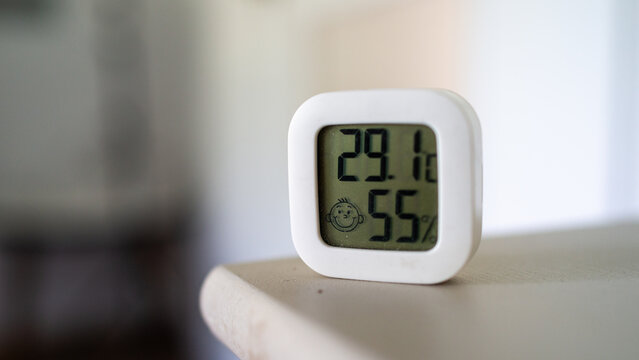Minimal indoor climate monitor on shelf showing temperature and humidity readings in soft natural light with shallow focus, clean neutral background, modern home comfort concept