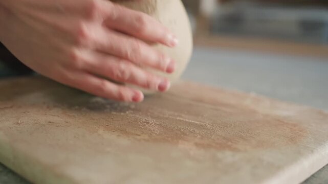 Clay lump on workboard potter kneads and wedges clay with steady hands, sandy residue across board, soft earthy texture, close up tactile studio process inside pottery workshop, intimate artisan