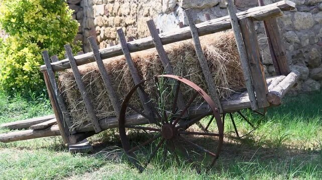 A rustic scene featuring a wagon loaded with hay sitting next to a stone wall in a green meadow