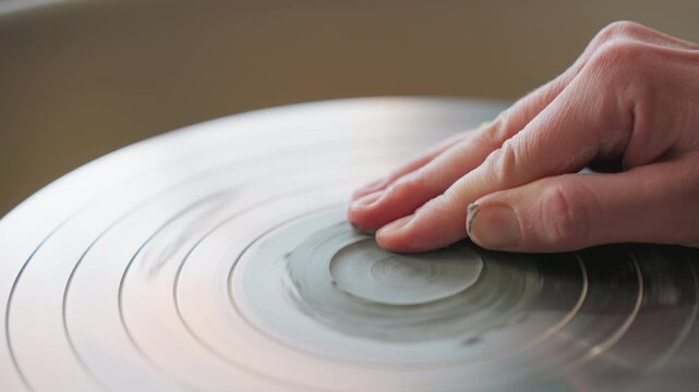 Fingertip smoothing wet clay on spinning wheel, white instructor demonstrates delicate centering and surface polishing, soft reflections on wheel, focused controlled motion for refined finish