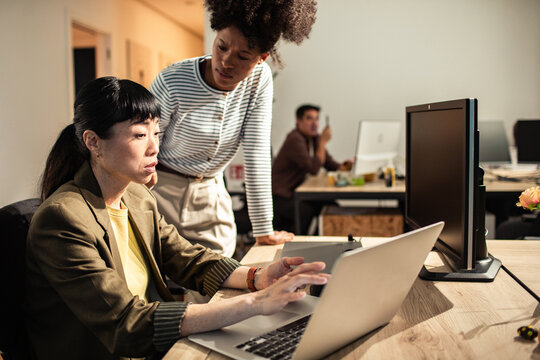 Two coworkers collaborating on laptop in modern office