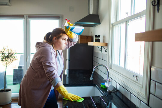 Tired woman cleaning kitchen countertop at home