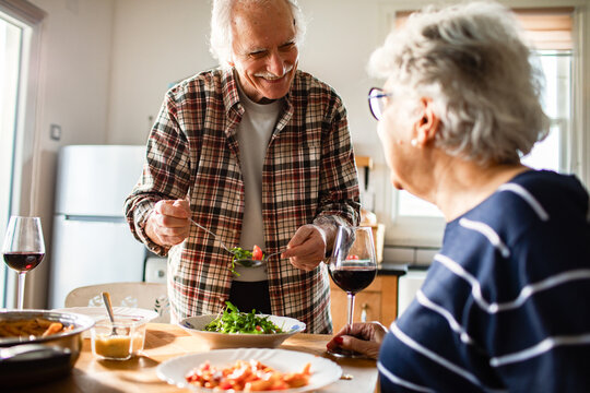 Senior couple sharing salad and wine at home kitchen