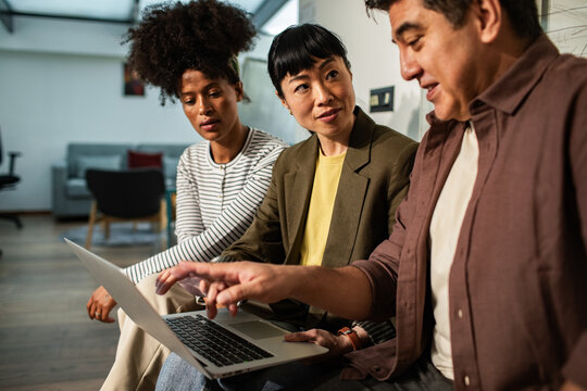 Three coworkers collaborating on laptop in modern office