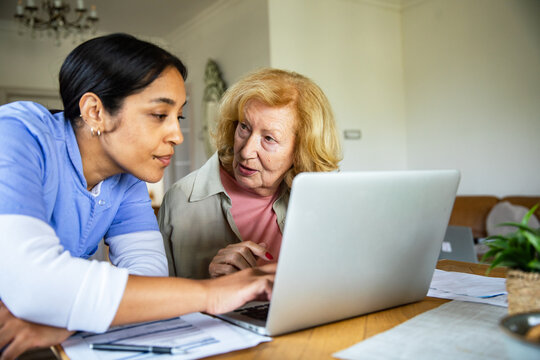 Caregiver helping senior woman use laptop at home