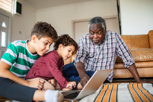 Grandfather helping grandsons with laptop at home