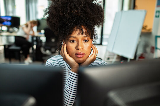 Young woman concentrating at dual monitors in modern office