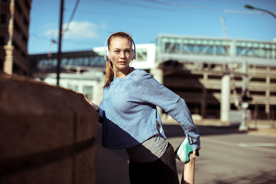 Woman runner stretching with headphones on city street